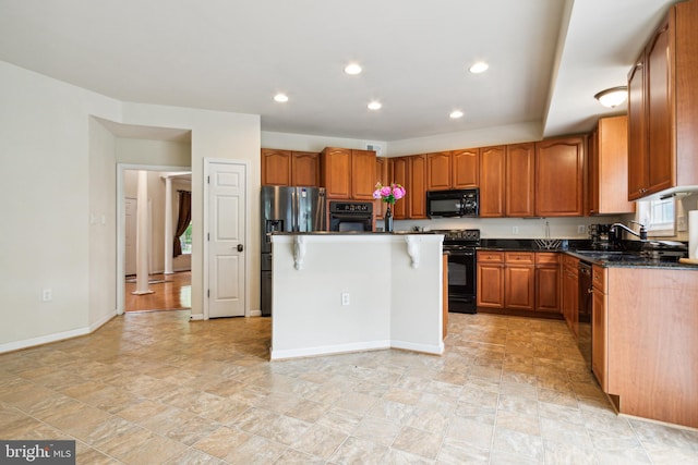 kitchen with a breakfast bar area, dark stone counters, sink, black appliances, and a center island