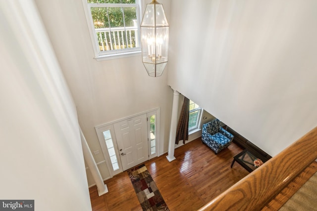 entryway with a towering ceiling, a chandelier, wood-type flooring, and plenty of natural light