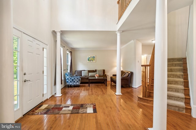 foyer entrance featuring ornate columns, hardwood / wood-style flooring, a towering ceiling, and ornamental molding