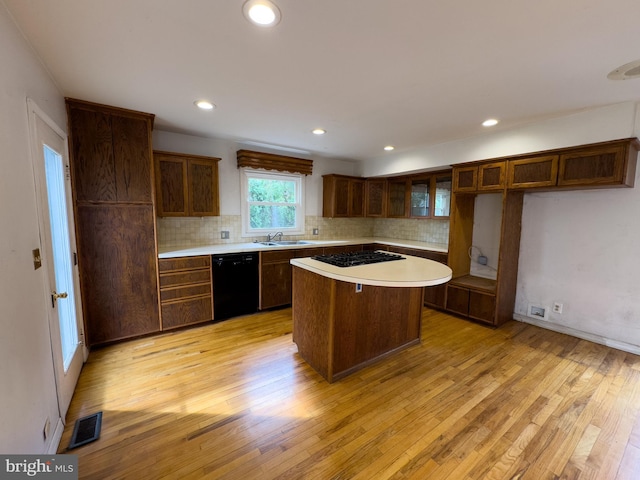 kitchen featuring white gas stovetop, a kitchen island, black dishwasher, sink, and light wood-type flooring