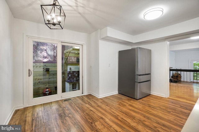 kitchen featuring a notable chandelier, hanging light fixtures, hardwood / wood-style floors, and stainless steel fridge