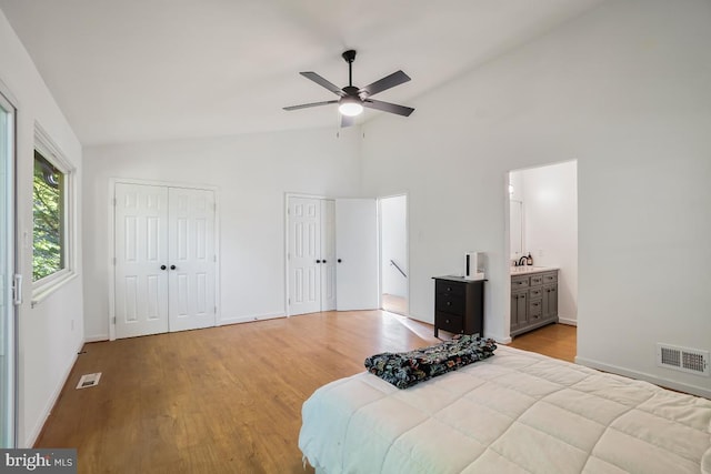 bedroom with light wood-type flooring, ceiling fan, connected bathroom, high vaulted ceiling, and two closets