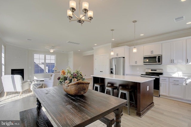 dining area with light hardwood / wood-style floors, crown molding, a large fireplace, and ceiling fan with notable chandelier