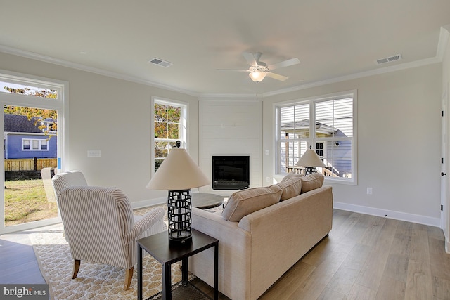 living room with ornamental molding, a fireplace, light hardwood / wood-style floors, and ceiling fan