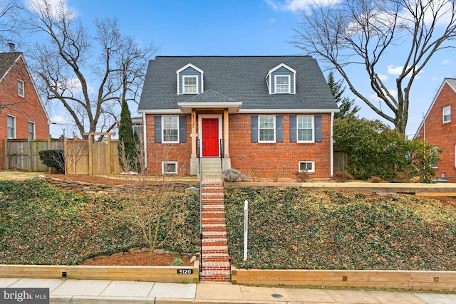 cape cod-style house featuring a fenced front yard, a shingled roof, and brick siding