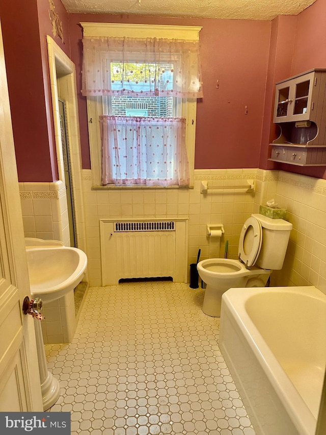 bathroom with radiator, toilet, a tub to relax in, and a textured ceiling