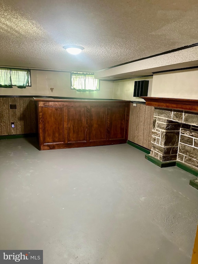 basement with wooden walls, a stone fireplace, and a textured ceiling