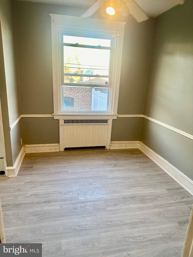 empty room with radiator, ceiling fan, vaulted ceiling, and light wood-type flooring