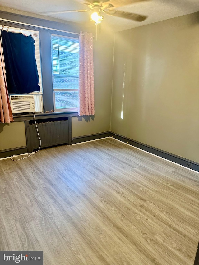 empty room featuring ceiling fan, light hardwood / wood-style flooring, cooling unit, and radiator