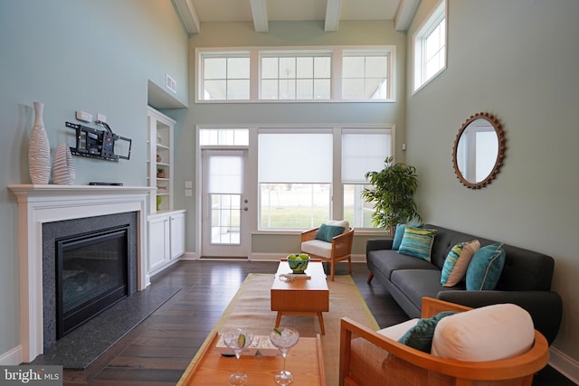 living room featuring a wealth of natural light, dark wood-type flooring, a high ceiling, and beam ceiling