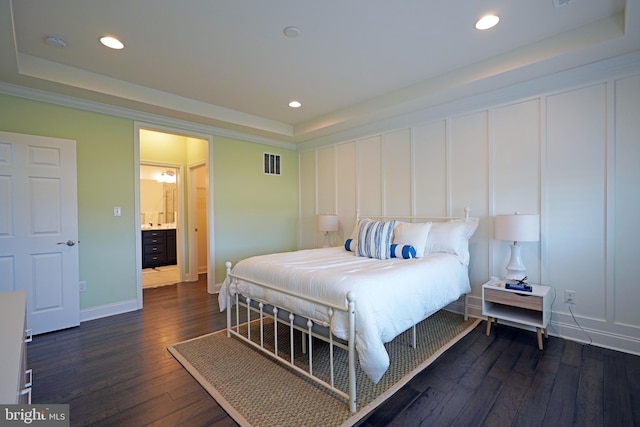 bedroom featuring ensuite bathroom, dark hardwood / wood-style flooring, and a raised ceiling