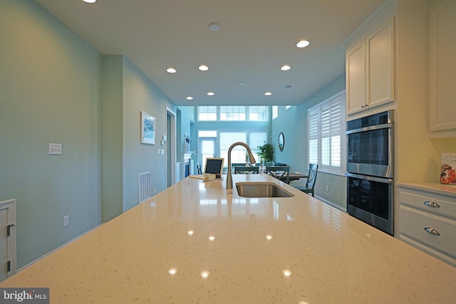 kitchen with stainless steel double oven, white cabinetry, sink, and light stone counters