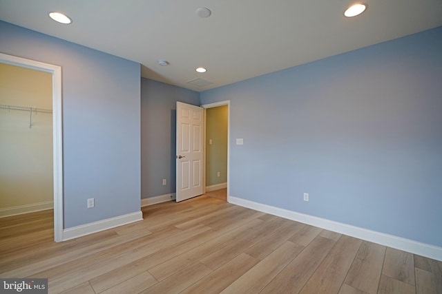 unfurnished bedroom featuring a closet, light wood-type flooring, and a spacious closet