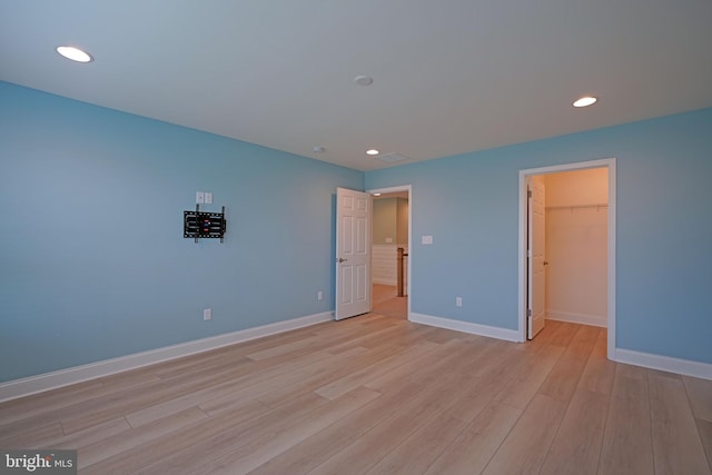 unfurnished bedroom with light wood-type flooring, a walk in closet, and a closet