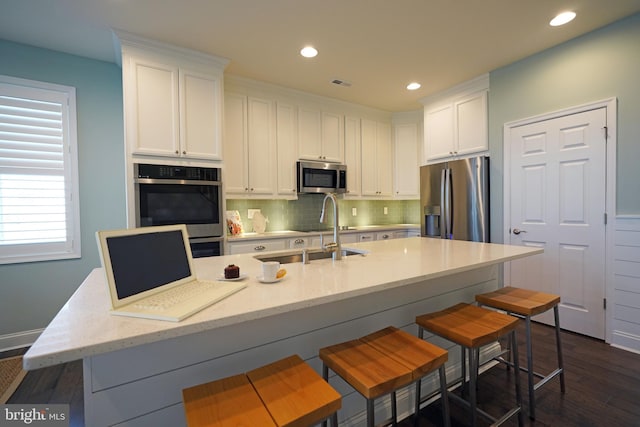 kitchen featuring stainless steel appliances, a kitchen bar, white cabinets, and dark wood-type flooring