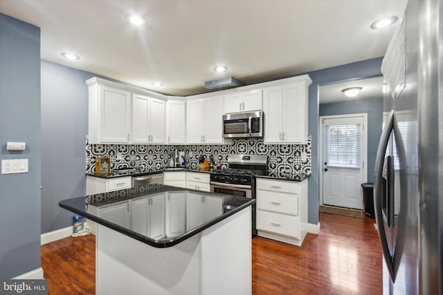 kitchen with appliances with stainless steel finishes, backsplash, white cabinets, a breakfast bar area, and dark hardwood / wood-style floors