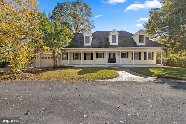 cape cod house featuring covered porch, an attached garage, and a front yard