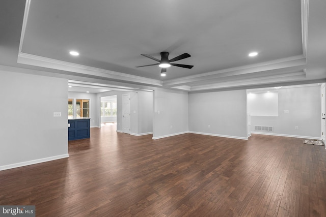 unfurnished living room with a ceiling fan, a tray ceiling, crown molding, visible vents, and dark wood-style flooring