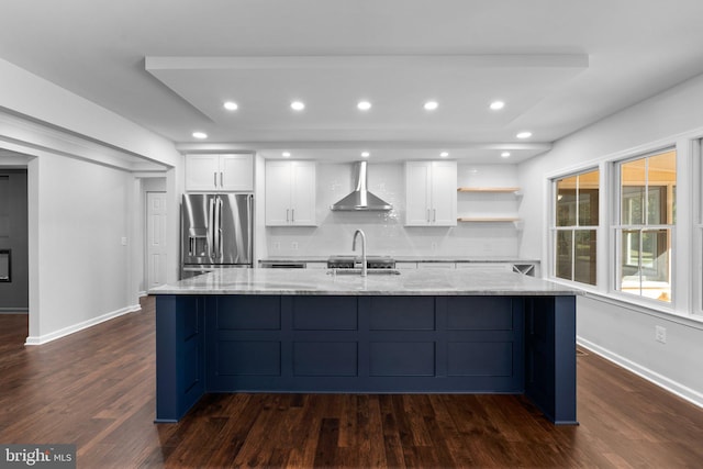 kitchen with white cabinets, stainless steel refrigerator with ice dispenser, wall chimney exhaust hood, light stone countertops, and dark hardwood / wood-style flooring