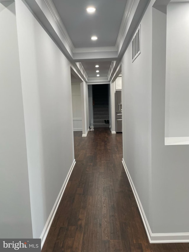 hallway with baseboards, ornamental molding, dark wood finished floors, visible vents, and a raised ceiling