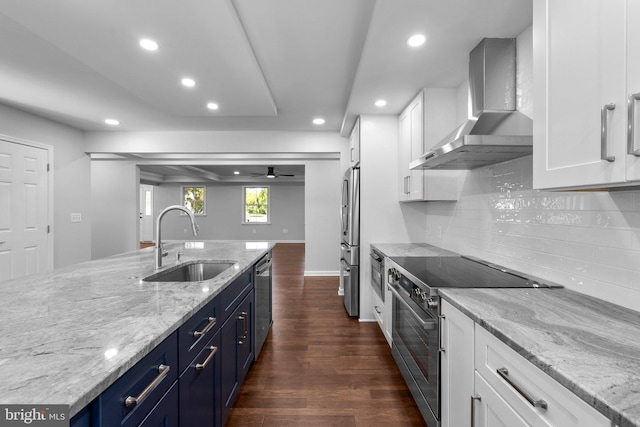kitchen with a sink, stainless steel appliances, wall chimney range hood, blue cabinetry, and recessed lighting