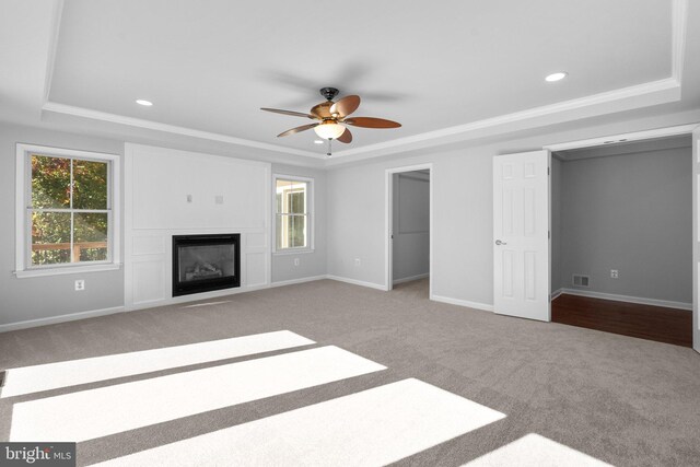 unfurnished living room featuring a raised ceiling, ceiling fan, light carpet, and ornamental molding