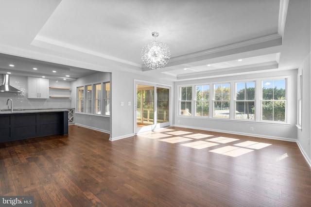 unfurnished living room featuring a raised ceiling, an inviting chandelier, dark wood-style floors, and a sink
