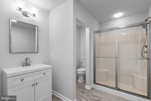 bathroom with toilet, wood-type flooring, a shower with door, and vanity