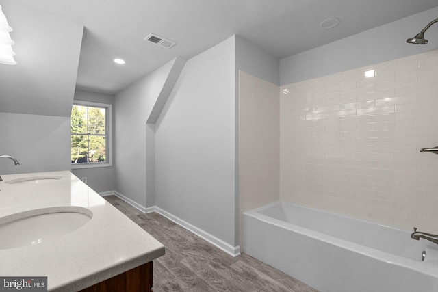 bathroom with hardwood / wood-style flooring, vanity, and tiled shower / bath