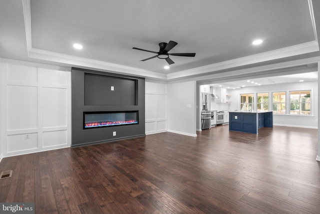 unfurnished living room featuring ceiling fan, a raised ceiling, dark hardwood / wood-style flooring, crown molding, and a fireplace