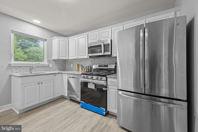 kitchen with appliances with stainless steel finishes, white cabinetry, light stone countertops, light hardwood / wood-style floors, and sink