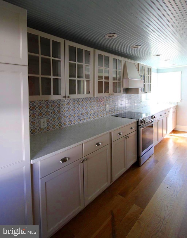 kitchen featuring decorative backsplash, hardwood / wood-style floors, electric range, custom exhaust hood, and white cabinets