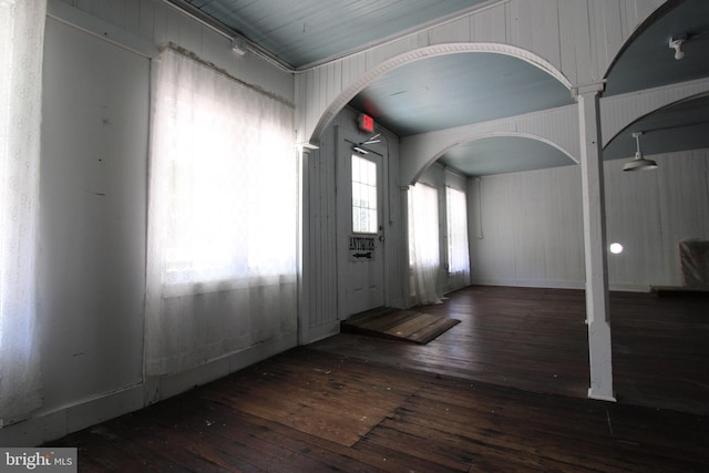 entryway featuring dark wood-type flooring, decorative columns, and wood walls