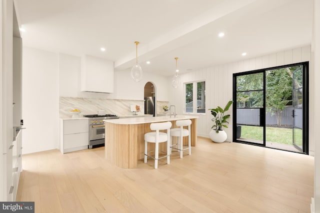 kitchen featuring white cabinets, a center island with sink, hanging light fixtures, and high quality appliances