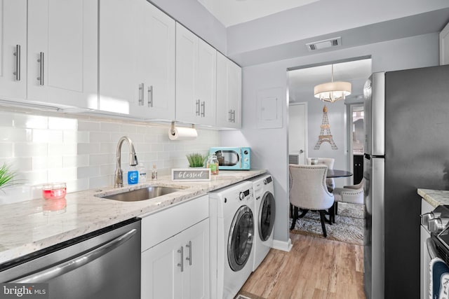 clothes washing area with washing machine and dryer, sink, and light wood-type flooring