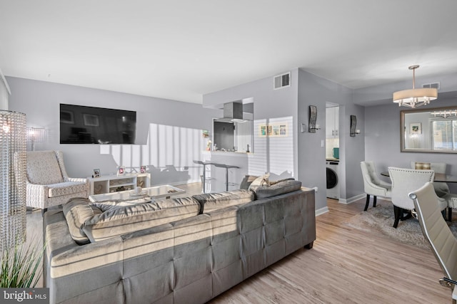 living room with plenty of natural light, washer / clothes dryer, a chandelier, and light wood-type flooring