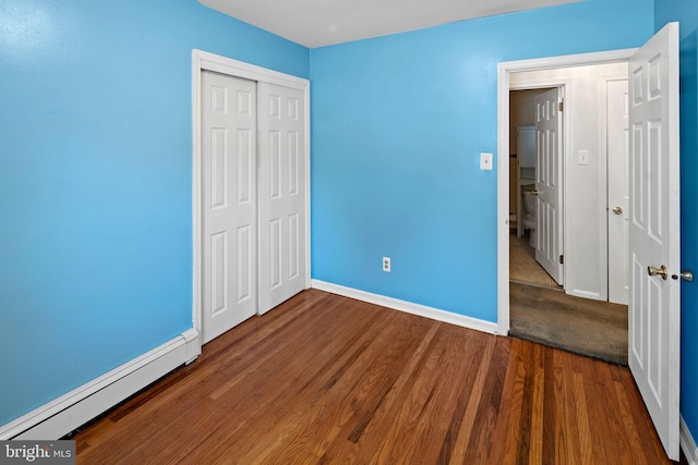 unfurnished bedroom with a closet, a baseboard heating unit, and dark hardwood / wood-style flooring