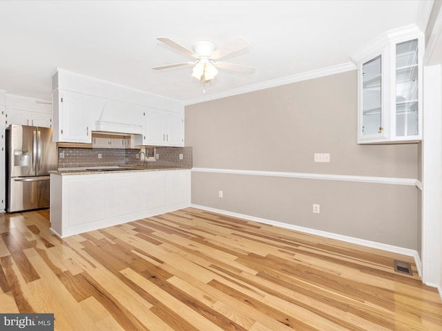 kitchen with stainless steel refrigerator with ice dispenser, kitchen peninsula, crown molding, decorative backsplash, and white cabinets