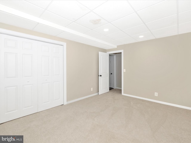 unfurnished bedroom with a drop ceiling, light carpet, and a closet