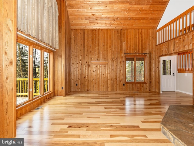 unfurnished living room featuring wood walls, light hardwood / wood-style floors, wood ceiling, and high vaulted ceiling