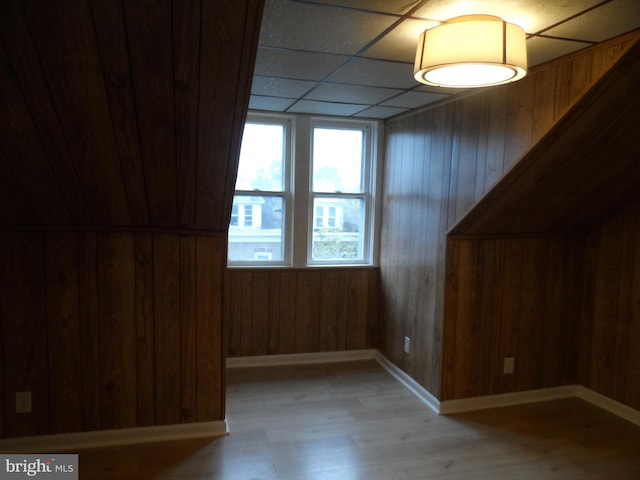 empty room with a paneled ceiling, wooden walls, and light wood-type flooring