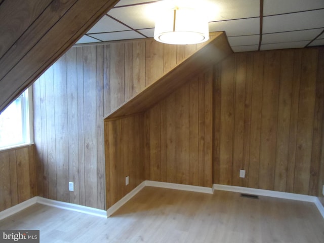 bonus room with light hardwood / wood-style flooring and wooden walls