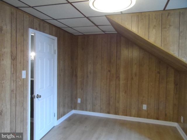 unfurnished room with hardwood / wood-style floors, a drop ceiling, and wooden walls