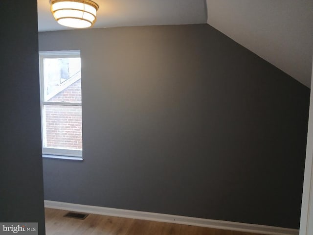 spare room featuring wood-type flooring and vaulted ceiling