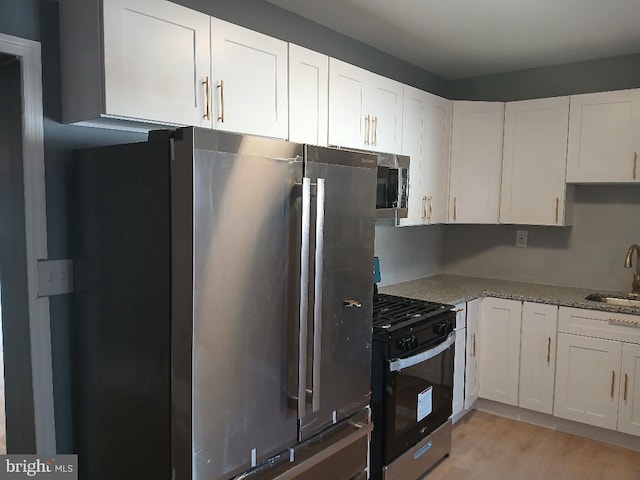 kitchen featuring white cabinets, appliances with stainless steel finishes, light stone countertops, and sink