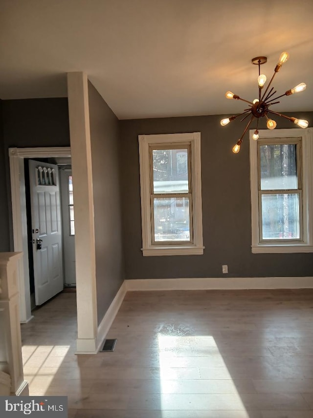 spare room with light wood-type flooring and a notable chandelier