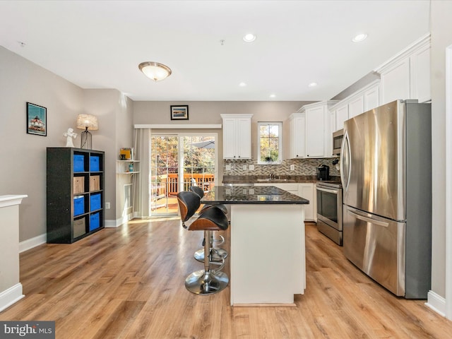 kitchen featuring tasteful backsplash, appliances with stainless steel finishes, light wood-type flooring, a kitchen island, and white cabinets