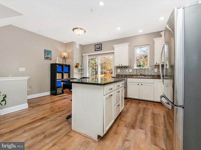 kitchen featuring stainless steel fridge, a breakfast bar area, white cabinetry, light hardwood / wood-style floors, and a center island