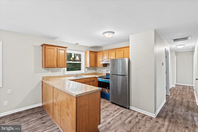 kitchen featuring sink, stainless steel appliances, light stone counters, light hardwood / wood-style flooring, and kitchen peninsula