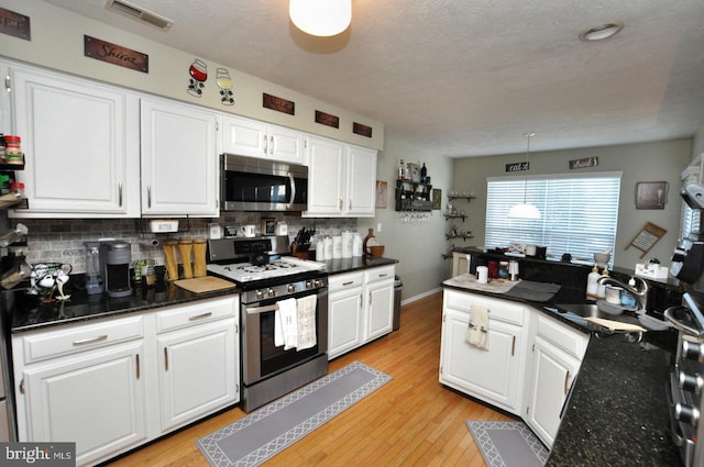 kitchen featuring stainless steel appliances, decorative backsplash, light wood-type flooring, and white cabinets